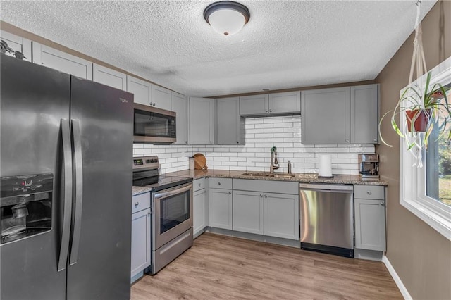 kitchen with dark stone counters, light hardwood / wood-style floors, stainless steel appliances, sink, and gray cabinets