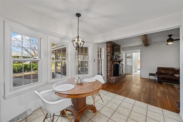 dining room featuring light tile patterned floors, a notable chandelier, visible vents, a brick fireplace, and beam ceiling