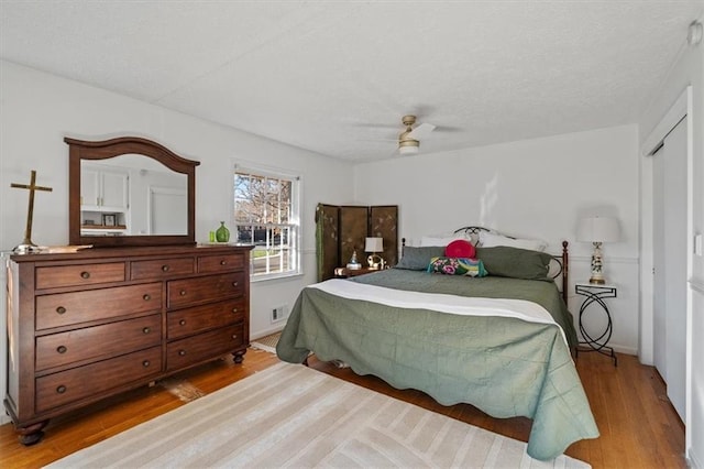 bedroom with a textured ceiling, wood finished floors, visible vents, baseboards, and a ceiling fan