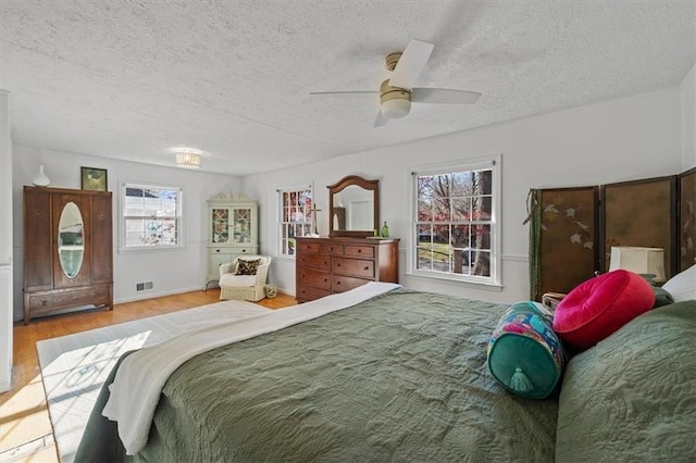 bedroom featuring a ceiling fan, visible vents, a textured ceiling, and wood finished floors