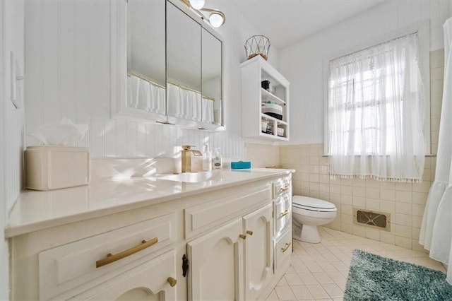 full bathroom with tile patterned flooring, toilet, vanity, tile walls, and wainscoting