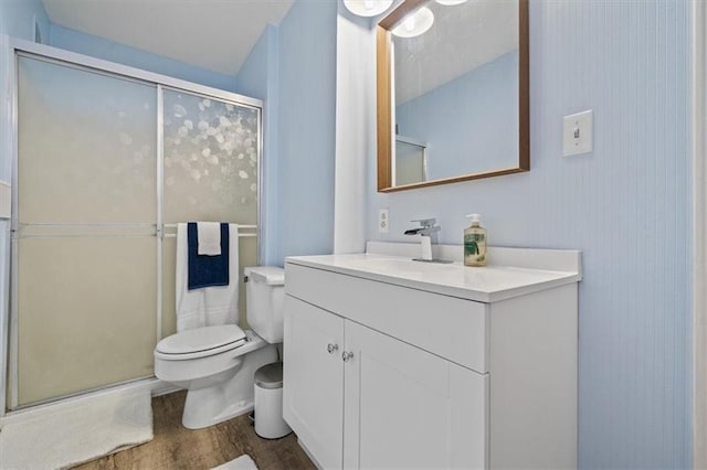 bathroom featuring wood finished floors, a stall shower, vanity, and toilet