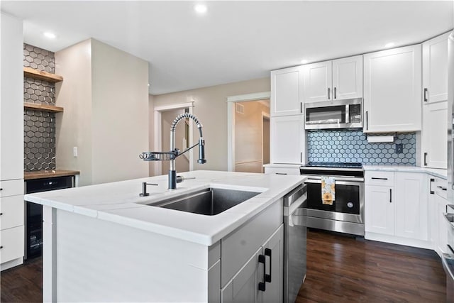 kitchen featuring white cabinets, sink, stainless steel appliances, and an island with sink