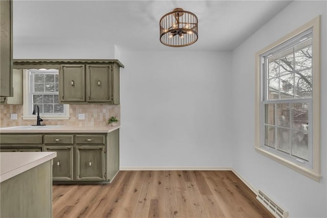 kitchen featuring backsplash, an inviting chandelier, green cabinetry, and sink