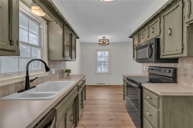 kitchen featuring backsplash, stainless steel dishwasher, sink, light hardwood / wood-style floors, and black / electric stove