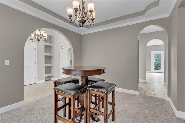 carpeted dining area featuring a raised ceiling, built in shelves, ornamental molding, and a notable chandelier