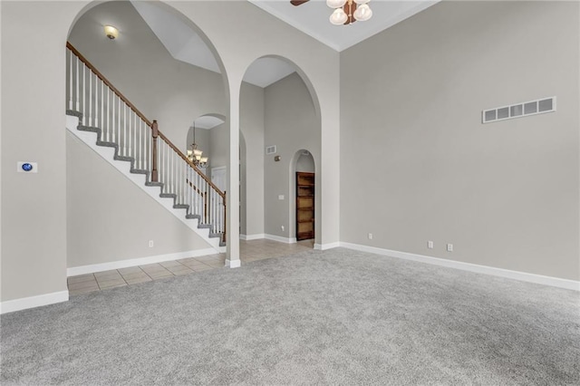 unfurnished living room with ceiling fan with notable chandelier, light carpet, and high vaulted ceiling