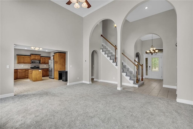 unfurnished living room with light carpet, high vaulted ceiling, and ceiling fan with notable chandelier