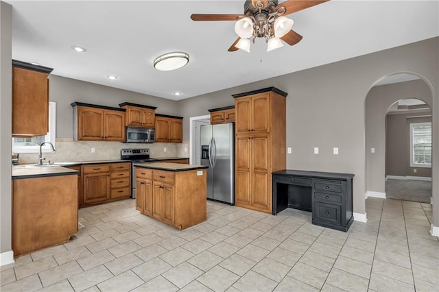 kitchen featuring ceiling fan, sink, backsplash, a kitchen island, and appliances with stainless steel finishes