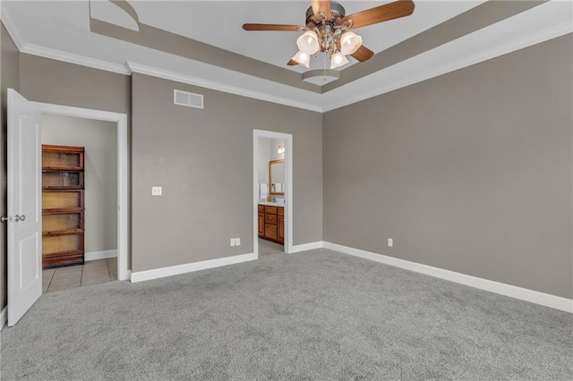 unfurnished bedroom featuring light carpet, ensuite bath, a raised ceiling, ceiling fan, and crown molding