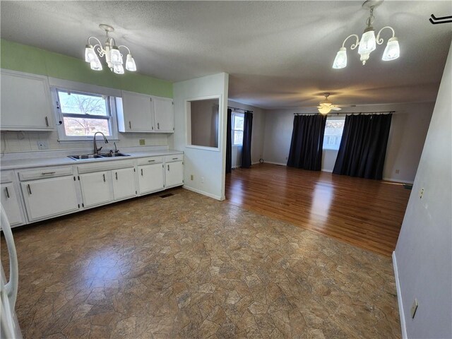 kitchen with sink, hanging light fixtures, wood-type flooring, white cabinets, and ceiling fan with notable chandelier