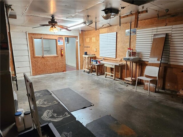 misc room with ceiling fan, concrete flooring, a workshop area, and wood walls