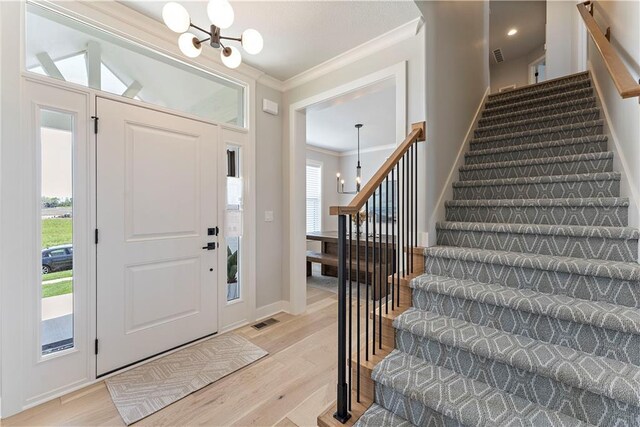 1516 NW 106th St, Kansas City, MO 64155 - entrance foyer featuring light wood finished floors, an inviting chandelier, visible vents, crown molding, and stairs
