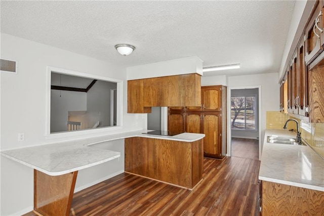 kitchen with sink, dark wood-type flooring, a kitchen breakfast bar, kitchen peninsula, and a textured ceiling