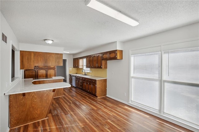 kitchen with sink, a textured ceiling, dark hardwood / wood-style flooring, kitchen peninsula, and a breakfast bar area