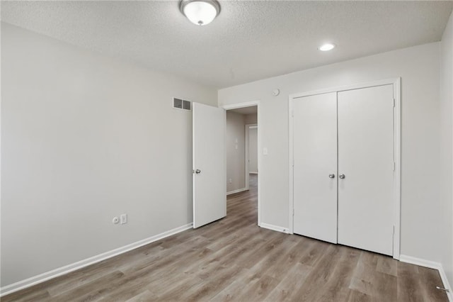 unfurnished bedroom with a textured ceiling, light hardwood / wood-style floors, and a closet