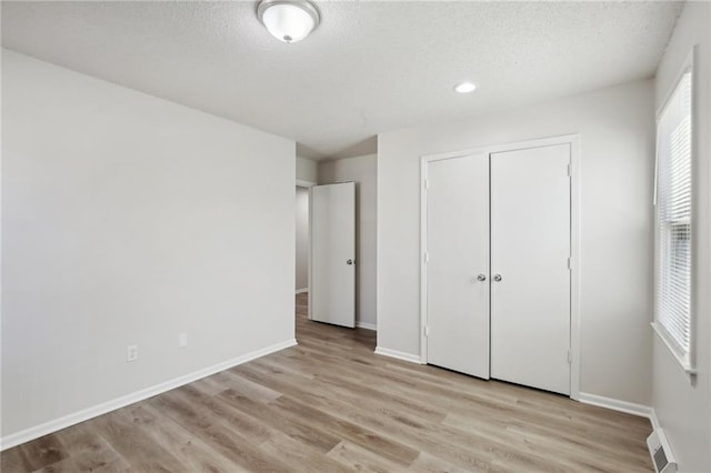 unfurnished bedroom featuring a closet, a textured ceiling, and light hardwood / wood-style flooring