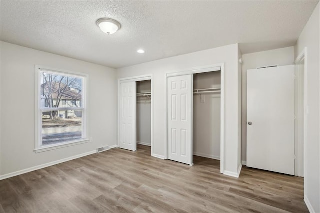 unfurnished bedroom featuring two closets, a textured ceiling, and light hardwood / wood-style floors