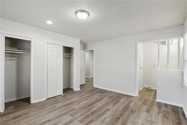 unfurnished bedroom featuring a textured ceiling, light hardwood / wood-style flooring, and two closets