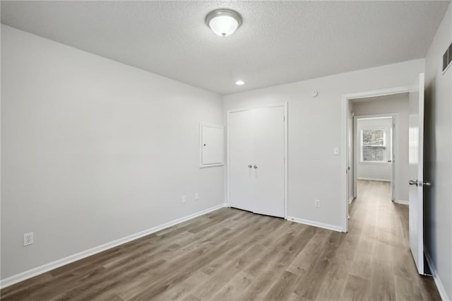 unfurnished bedroom featuring a closet, a textured ceiling, and light hardwood / wood-style flooring