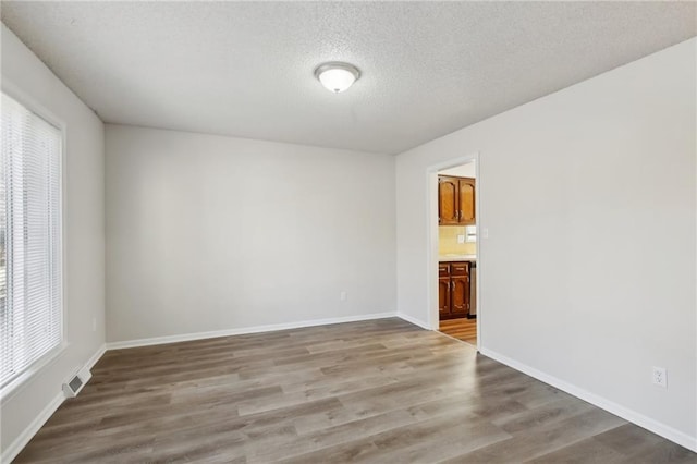 unfurnished room with light wood-type flooring and a textured ceiling