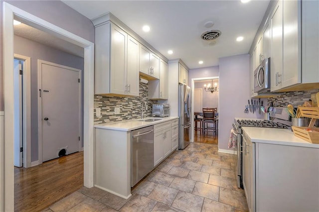 kitchen featuring white cabinetry, sink, backsplash, stainless steel appliances, and an inviting chandelier