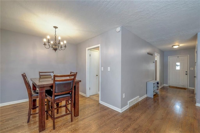 dining room with hardwood / wood-style flooring, a notable chandelier, and a textured ceiling