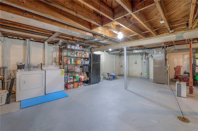 basement featuring heating unit, black refrigerator, water heater, and washing machine and clothes dryer