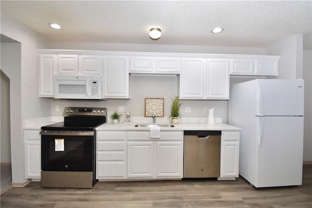 kitchen with light wood finished floors, stainless steel appliances, light countertops, white cabinetry, and a sink