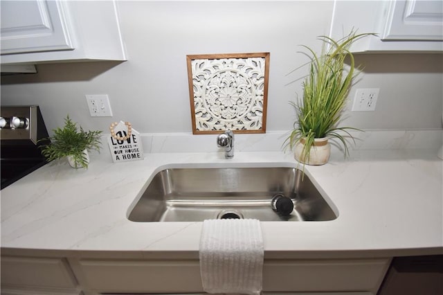 details featuring a sink, white cabinetry, and light stone countertops