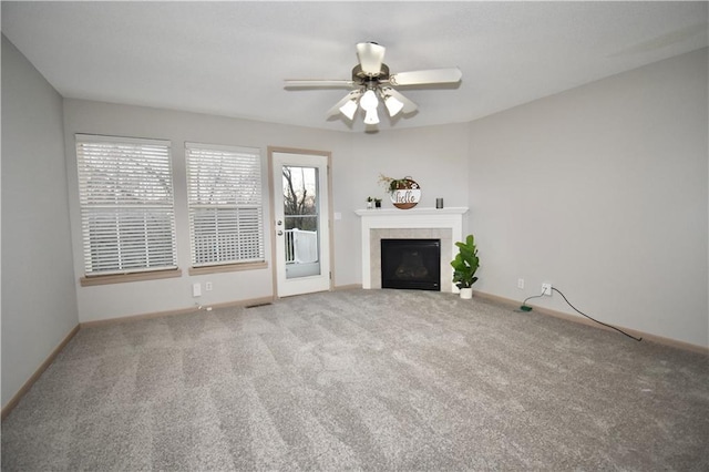 unfurnished living room featuring ceiling fan, carpet floors, a tile fireplace, and baseboards