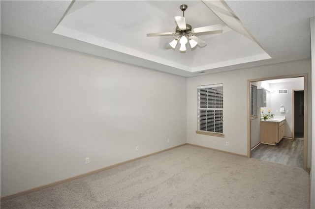 unfurnished room with ceiling fan, light carpet, visible vents, baseboards, and a raised ceiling