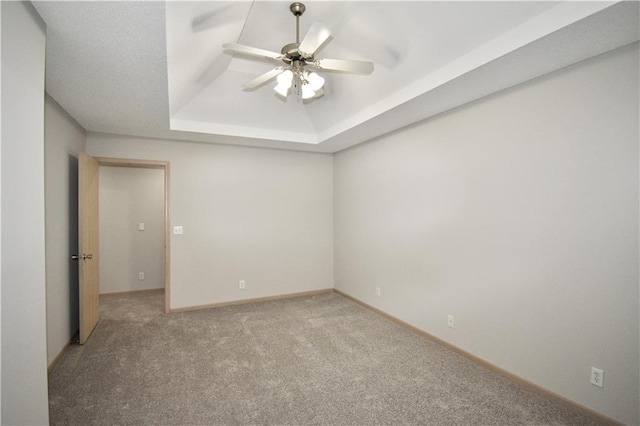 carpeted spare room with baseboards, a raised ceiling, and a ceiling fan