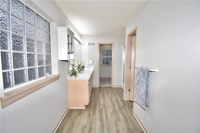 corridor featuring light wood-type flooring, visible vents, and baseboards