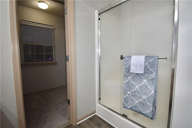 full bathroom featuring wood finished floors, a shower with door, and baseboards