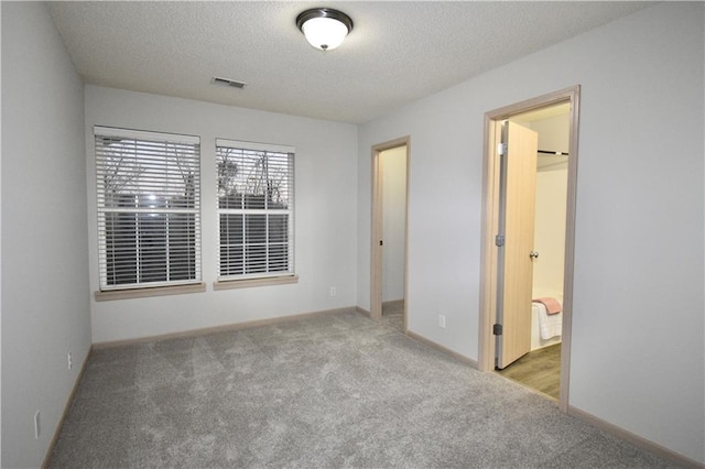 unfurnished bedroom featuring a textured ceiling, visible vents, and light colored carpet