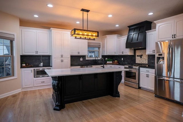 kitchen with white cabinets, light hardwood / wood-style flooring, hanging light fixtures, a center island with sink, and appliances with stainless steel finishes