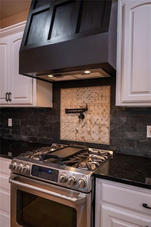 kitchen featuring stainless steel range with gas cooktop, white cabinets, backsplash, dark stone counters, and premium range hood