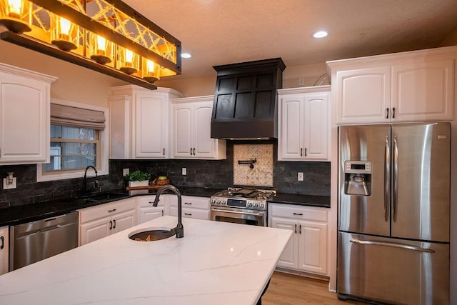 kitchen with premium range hood, white cabinets, dark stone counters, appliances with stainless steel finishes, and sink