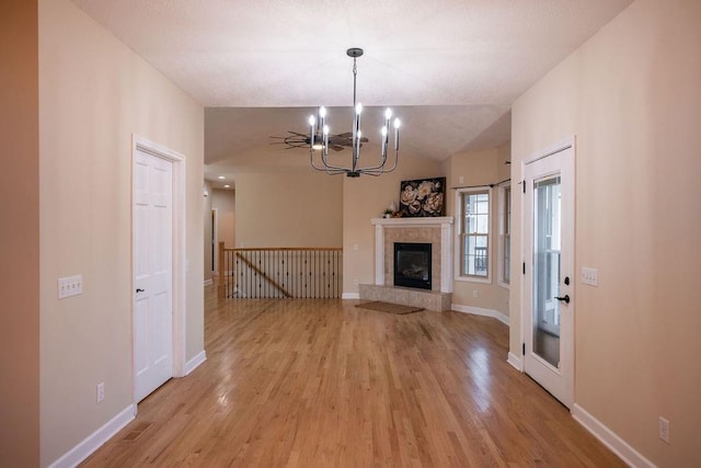 unfurnished living room with light wood-type flooring, a tiled fireplace, vaulted ceiling, and an inviting chandelier