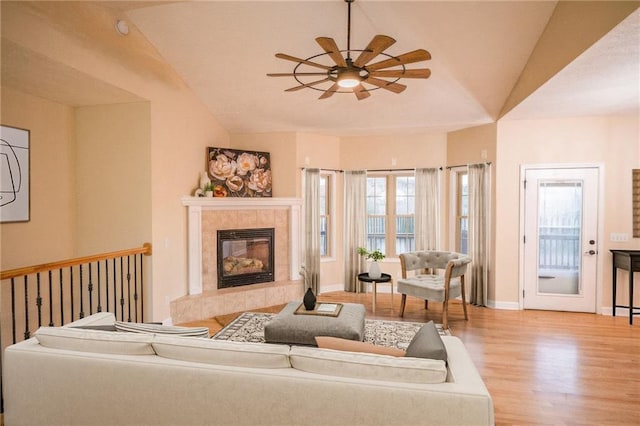 living room with a tiled fireplace, ceiling fan, light hardwood / wood-style floors, and vaulted ceiling