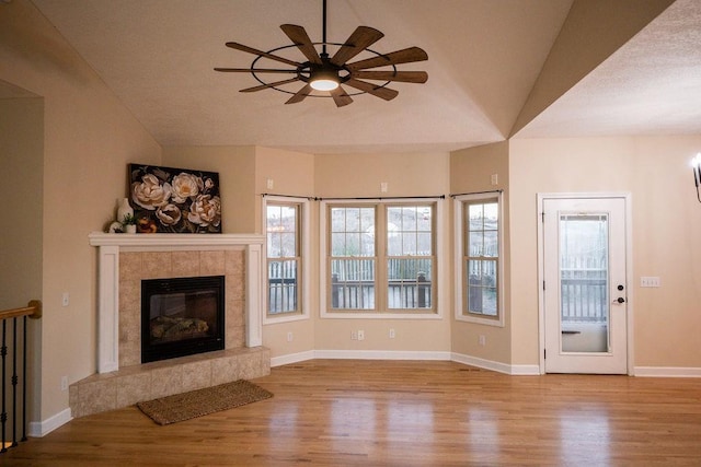 unfurnished living room featuring a tile fireplace, light wood-type flooring, ceiling fan, and vaulted ceiling