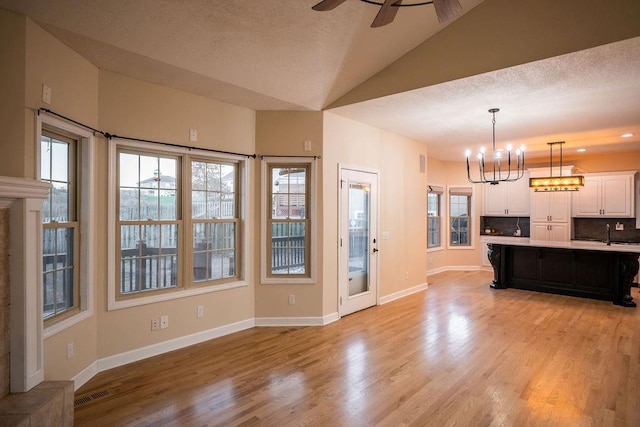 kitchen with white cabinets, lofted ceiling, ceiling fan with notable chandelier, decorative backsplash, and a kitchen island