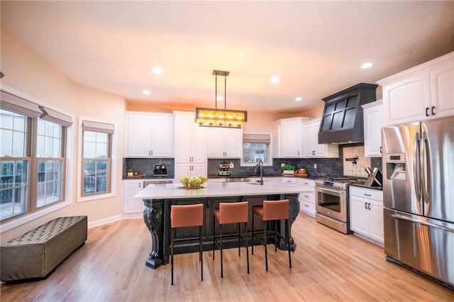 kitchen with hanging light fixtures, stainless steel appliances, an island with sink, white cabinetry, and a kitchen breakfast bar