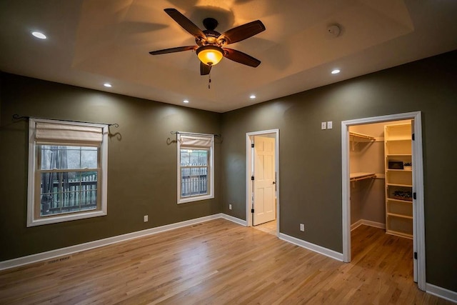 unfurnished bedroom with a walk in closet, a closet, ceiling fan, and light hardwood / wood-style floors