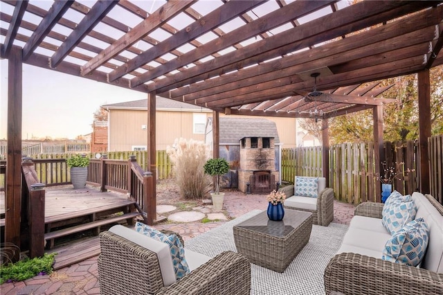 patio terrace at dusk with a pergola, a wooden deck, and an outdoor living space with a fireplace