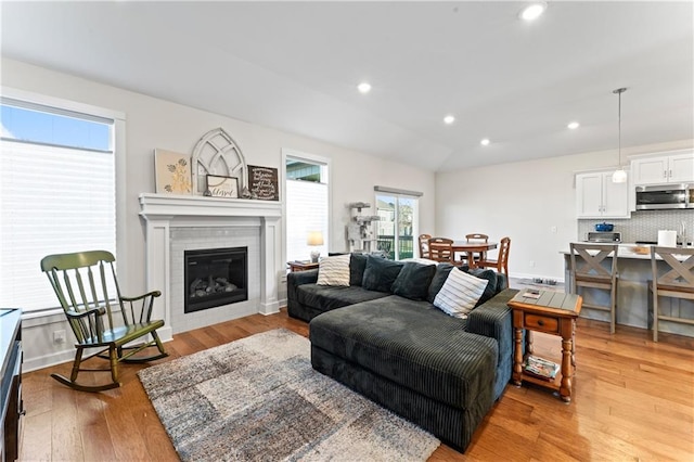 living room with a tiled fireplace, light hardwood / wood-style flooring, and vaulted ceiling