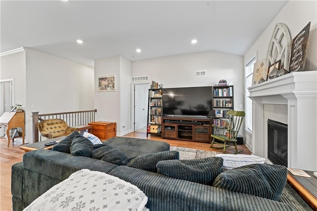 living room featuring hardwood / wood-style flooring, vaulted ceiling, and a tiled fireplace