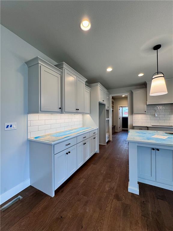 7601 NE 103rd Ter, Kansas City, MO 64157 - kitchen with baseboards, light countertops, dark wood-type flooring, tasteful backsplash, and pendant lighting