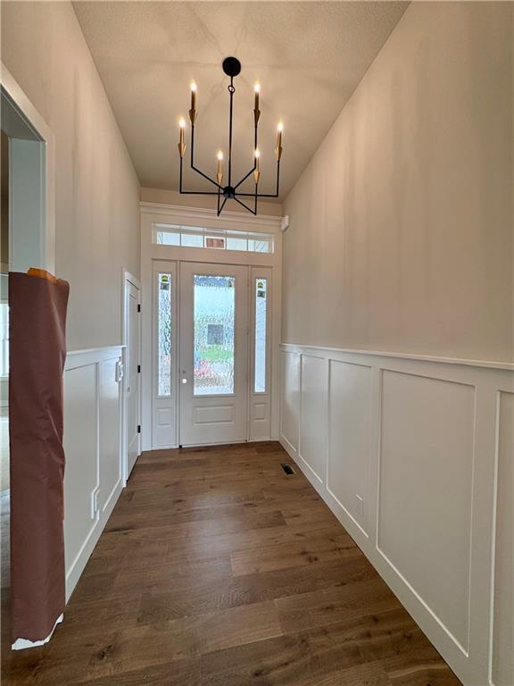 7719 NE 103rd Ter, Kansas City, MO 64157 - foyer with a decorative wall, a chandelier, dark wood-style flooring, and wainscoting